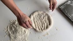 a person is kneading dough on a white counter with a baking pan in the background