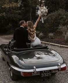 a bride and groom are sitting in the back of a convertible car with their hands up