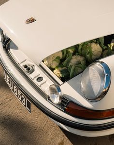 the front end of a white car with flowers in it's trunk and hood