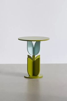 a round table with two leaves on it and a green base, against a white wall