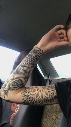 a woman with tattoos on her arm sitting in the back seat of a car and holding her hand up to her face