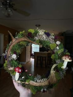 a hand holding up a wreath with mushrooms and moss