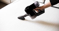 a person using a vacuum to clean a mattress with the help of a hand held vacuum