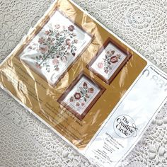 two cross stitch kits sitting on top of a white doily covered table with lace