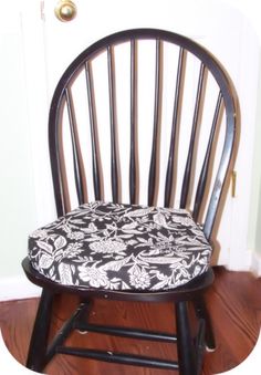 a wooden chair with a black and white floral seat pad sitting on top of a hard wood floor