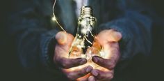 a man holding a light bulb in his hands with some string lights around the bulbs