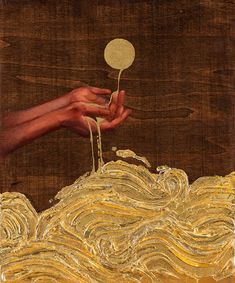 a painting with gold paint on it and a hand holding a ball above the water