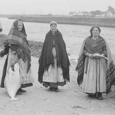 three women are standing by the water with their heads wrapped in scarves and shawls