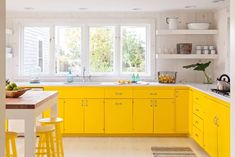 a kitchen with yellow cabinets and stools in front of the counter top, along with white walls