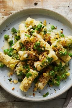 a white plate topped with pasta and broccoli covered in seasoning on top of a wooden table