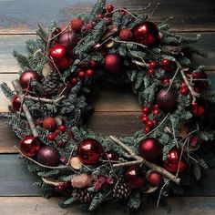 a christmas wreath with red ornaments and pine cones on a wooden background, top view