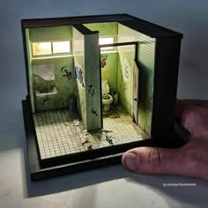 a person holding up a small model of a bathroom