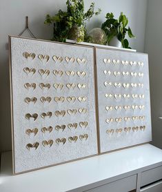 two pieces of paper with hearts on them sitting on top of a white shelf next to a potted plant