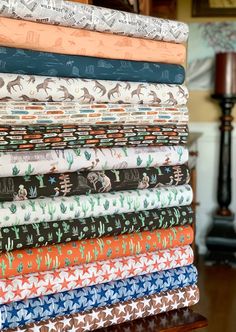 a stack of different colored fabrics sitting on top of a wooden table next to a lamp