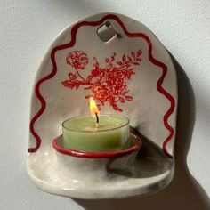 a candle is lit in a small bowl on a wall mounted plate with a red and white floral design