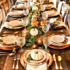 a table set for thanksgiving dinner with pumpkins and greenery