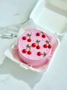 a pink cake with cherries on it in a box