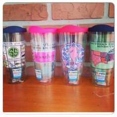 three different colored cups sitting on top of a wooden table next to a brick wall