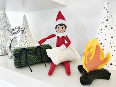 an elf is sitting next to a campfire and some knitted items on a shelf