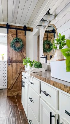 a kitchen with white cabinets and wooden doors on the wall, surrounded by potted plants