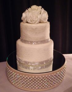 a three tiered wedding cake with white roses on top and crystal trimmings