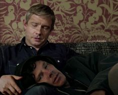 a man laying on top of a couch next to another man with his eyes closed