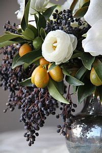 a vase filled with white flowers and oranges on top of a table next to a wall