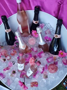 several bottles of wine are in an ice bucket with pink flowers on the rim and petals around them