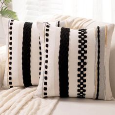 two black and white pillows sitting on top of a couch next to a plant in a vase