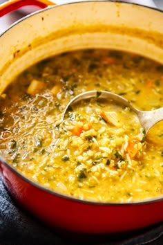 a red pot filled with soup on top of a stove next to a wooden spoon