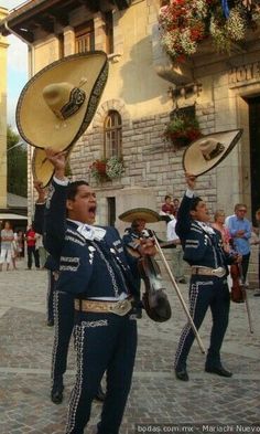 a group of men in uniform playing musical instruments on a cobblestone street while people watch