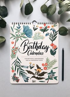 the birthday calendar is surrounded by greenery and leaves on a gray surface with a black pen