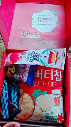 an open red box filled with snacks and other items on a table next to a person's hand