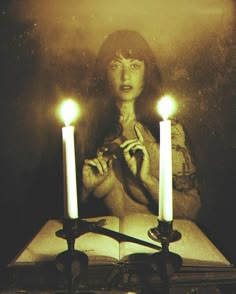 a woman sitting at a table with three candles in front of her and an open book behind her