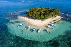 an island with several boats in the water and palm trees on one side, surrounded by clear blue water