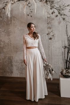 a woman standing in front of a white wall wearing a long sleeved wedding dress