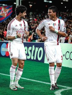 two men in white uniforms standing on a soccer field with their arms around each other