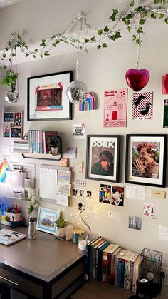 a desk with many pictures and plants hanging from it's wall above the desk