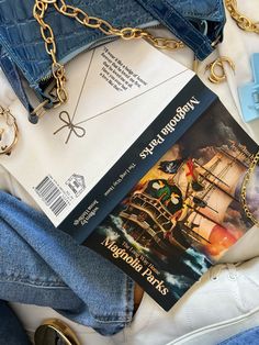 an open book and some blue jeans on top of a white surface with gold chains