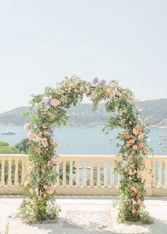 an outdoor ceremony setup with flowers and greenery on the side of a balcony overlooking water