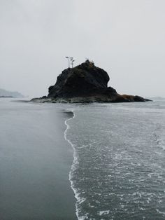 an island in the middle of the ocean on a foggy day with waves coming in