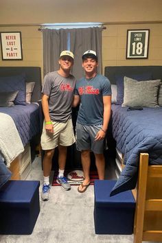 two young men standing next to each other in a room with beds and blue sheets