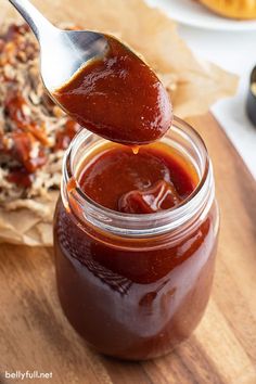 a spoon full of bbq sauce sitting on top of a wooden cutting board next to other food