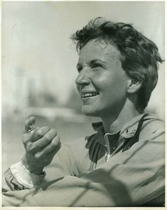 an old black and white photo of a woman holding something up to her face while smiling