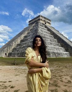 a woman standing in front of an ancient pyramid with her arms crossed and looking at the camera