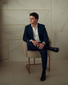 a man in a suit and tie sitting on a chair with his legs crossed, looking off to the side