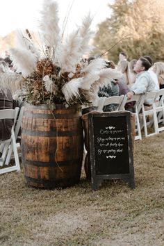 a wooden barrel with some white flowers in it next to a chalkboard sign and chairs