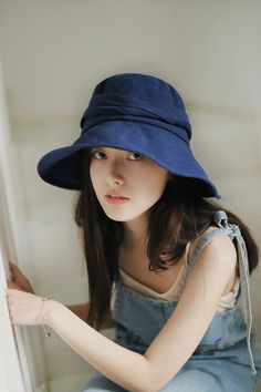 a young woman wearing a blue hat sitting on the edge of a window sill