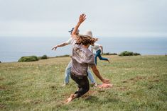 three people are playing frisbee in the grass by the ocean on a cloudy day