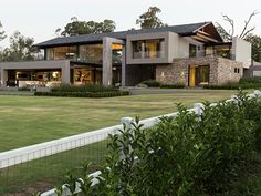 a large house sitting in the middle of a lush green field next to a white fence